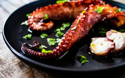 Tentacules de poulpe grillés, parsemés de persil frais, prêts à être dégustés. Une recette poulpe simple et savoureuse.