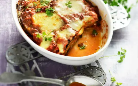 Un plat de recette parmigiana napolitaine gratinée, avec des aubergines, de la sauce tomate et du fromage fondant, garni de persil frais.