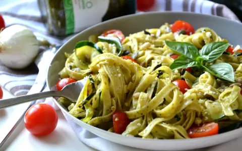 Un plat de tagliatelles de courgettes, tomates cerises et pesto, garni de basilic frais et de pignons de pin.