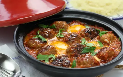 Un savoureux tajine kefta avec des boulettes de viande et des œufs pochés dans une sauce tomate épicée, garni de persil frais.