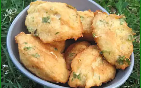 Un bol rempli de beignets de morue portugais dorés, parsemés d'herbes vertes, sur un fond d'herbe.