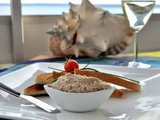 Un bol de rillettes de maquereau, servi avec des toasts grillés, une tomate cerise et un verre de vin blanc.