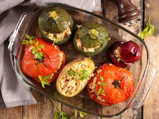 Plat de farce à légume : tomates, courgettes rondes, oignon rouge et pomme de terre farcis de grains, joliment présentés dans un plat en verre.