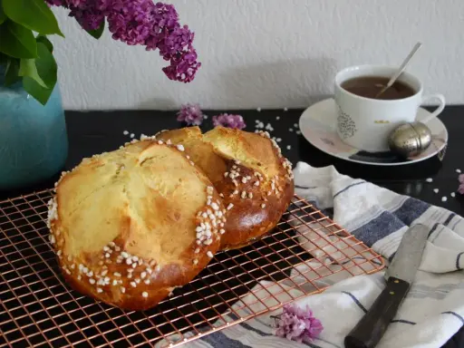 Deux pains briochés, parfaits pour une mouna recette, refroidissent sur une grille. Une tasse de thé et des lilas complètent la scène.