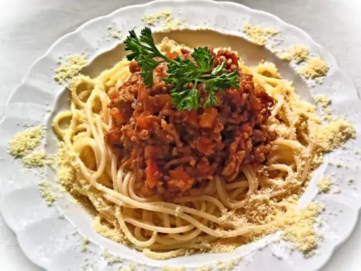 Une assiette de spaghetti bolognaise italienne, garnie de persil frais et de parmesan râpé. Un délice pour les amateurs de cuisine italienne.