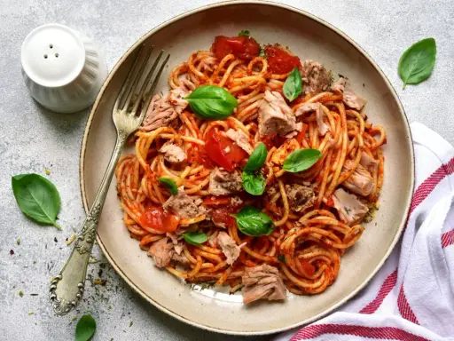 Assiette de pâtes au thon, sauce tomate et basilic frais. Un plat simple et savoureux prêt à être dégusté.