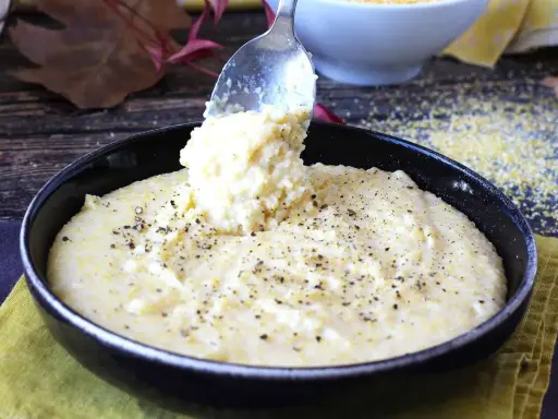 Une cuillère sert une portion généreuse de polenta crémeuse, assaisonnée de poivre noir, dans un bol. Une recette polenta réconfortante.
