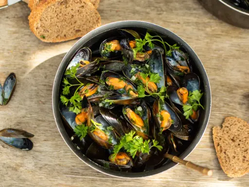 Un plat généreux de moules marinières, garni de persil frais, avec du pain de campagne à côté.