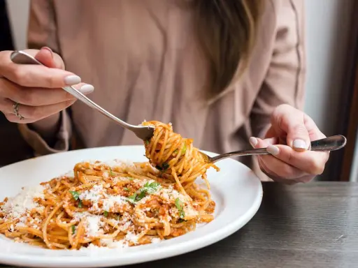 Une personne mange des spaghettis à la sauce tomate et au parmesan avec deux fourchettes.