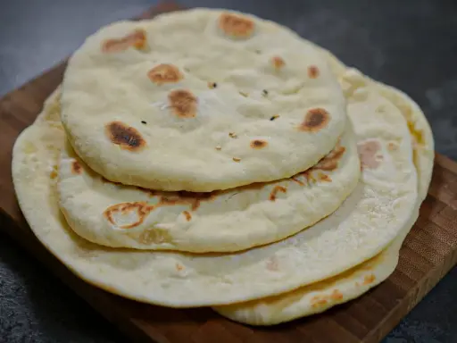 Pile de pains arabes moelleux, légèrement dorés par la cuisson, sur une planche en bois. Parfait pour accompagner un repas.