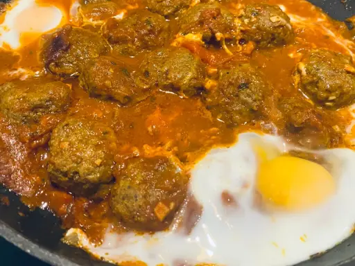 Un plat de tajine kefta oeuf mijote dans une sauce tomate épicée, avec des œufs pochés.