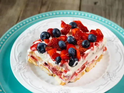 Tranche de tiramisu aux fruits rouges, garnie de fraises et myrtilles fraîches, sur une assiette blanche ornée.