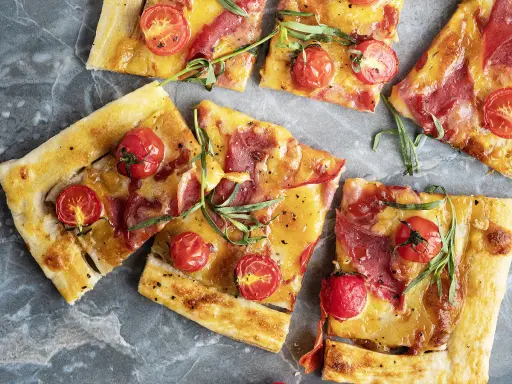 Délicieuse recette salée avec pâte filo : tartes fines garnies de tomates cerises, fromage fondant et fines tranches de charcuterie, parsemées d'herbes fraîches.