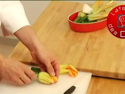 Préparation d'une fleur de courgette recette. Des mains préparent des fleurs de courgette sur une planche à découper.