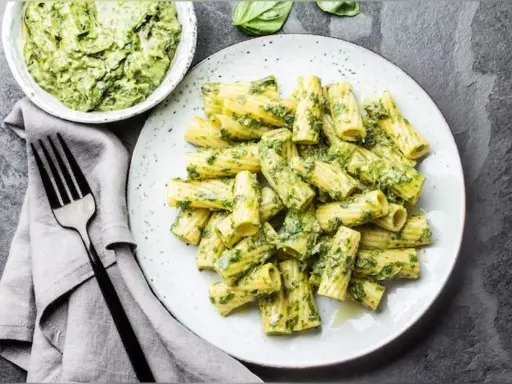 Assiette de pâtes rigatoni généreusement enrobées de pesto vert vif, avec un bol de sauce à côté. Un délice de pâtes au pesto !