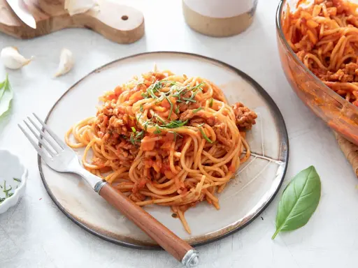 Une assiette de spaghetti à la bolognaise, plat réconfortant de one pot pasta, garnie d'herbes fraîches.