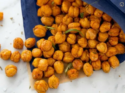 Un tas de pois chiches grillés dorés, certains tombant d'un sac bleu, avec des brins de romarin.