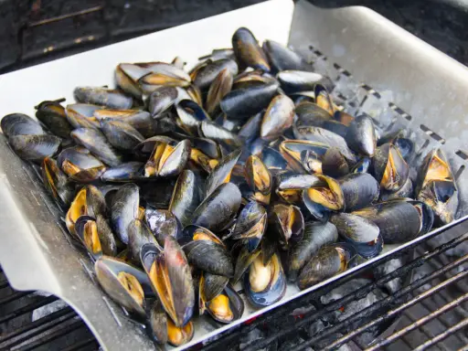 Un plateau de moules au barbecue, prêtes à être dégustées. Les coquilles sombres et orangées s'entrouvrent sous l'effet de la chaleur.