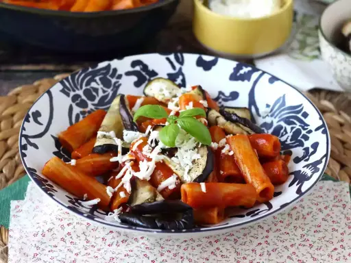 Pâtes rigatoni généreusement garnies de sauce tomate, d'aubergines grillées et de fromage râpé, le tout surmonté d'une feuille de basilic frais. Un plat de pâtes aubergines appétissant.