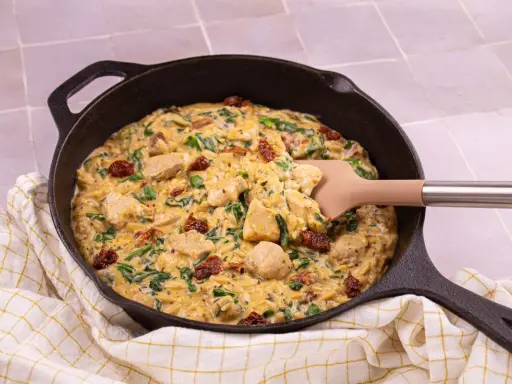 Un plat réconfortant de one pot orzo avec poulet, épinards et tomates séchées, servi dans une poêle en fonte.