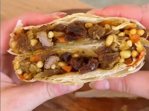 Une délicieuse pastilla agneau, coupée en deux, révèle sa garniture généreuse de viande, raisins secs, pignons et carottes.