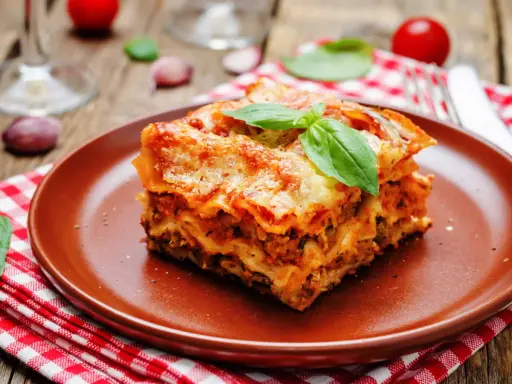 Une part généreuse de lasagne végétarienne, dorée au four, garnie de basilic frais, sur une assiette en terre cuite.