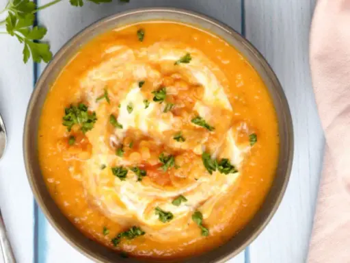 Un bol de soupe crémeuse aux lentilles corail, garni de crème et de persil frais, prêt à être dégusté avec une cuillère.
