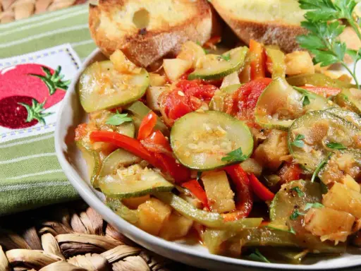 Un plat de légumes mijotés, rappelant un pisto manchego, avec des courgettes, poivrons et tomates, servi avec des toasts grillés.