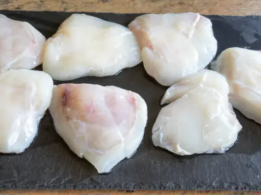 Plusieurs morceaux de lotte crue, prêts pour une cuisson au four, sont disposés sur une planche d'ardoise.