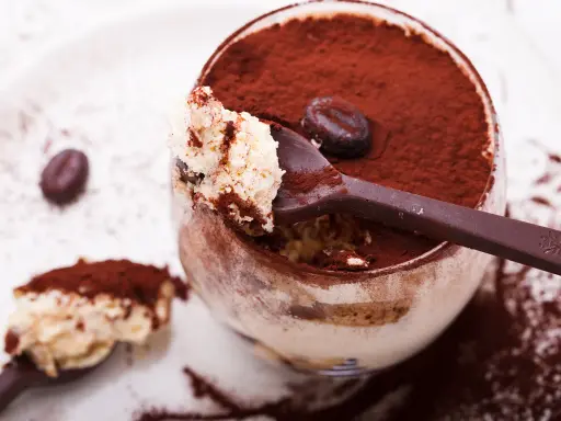 Un déliceux tiramisu cacao, saupoudré de cacao, avec une cuillère pleine de crème onctueuse et un grain de café.
