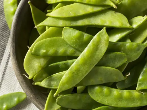 Un bol en bois rempli de pois gourmands frais, prêts pour la cuisson.