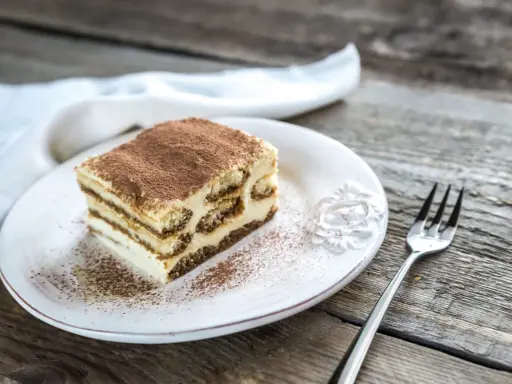 Une part de tiramisu maison, saupoudrée de cacao, sur une assiette blanche, prête à être dégustée. La conservation de ce délice est essentielle pour en savourer chaque bouchée.