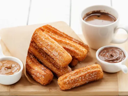 Churros dorés et croustillants, saupoudrés de sucre, prêts à être trempés dans le chocolat. Une recette gourmande pour un goûter parfait.