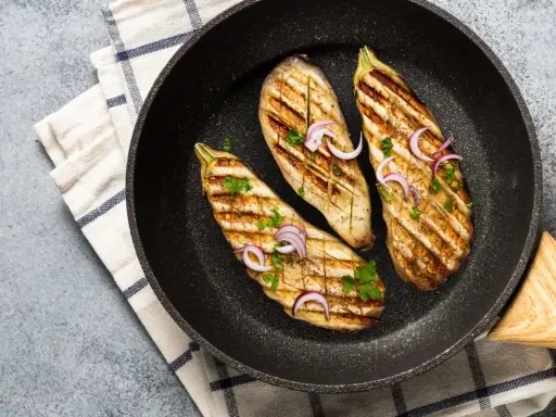 Aubergines grillées dans une poêle, garnies d'oignons rouges et de persil. Une délicieuse recette aubergine prête à être dégustée.