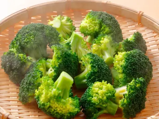 Brocolis coupés en bouquets dans un panier en osier, prêts pour la cuisson. La vapeur s'échappe, signe d'une cuisson à la vapeur parfaite.