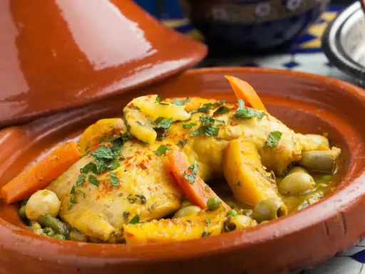 Un plat de tajine recette traditionnelle, avec du poulet, des carottes, des olives et des abricots, garni de persil frais.