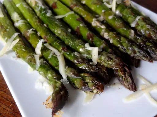 Un plat d'asperges au four, tendres et légèrement grillées, parsemées de copeaux de parmesan. Un délice simple et savoureux.