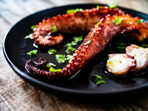Tentacules de poulpe grillés, parsemés de persil frais, prêts à être dégustés. Une recette poulpe simple et savoureuse.