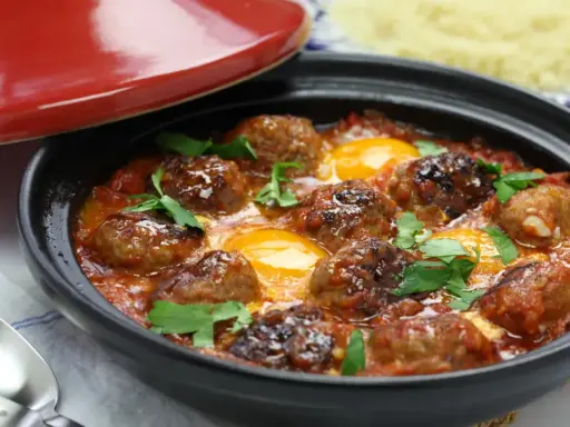 Un savoureux tajine kefta avec des boulettes de viande et des œufs pochés dans une sauce tomate épicée, garni de persil frais.