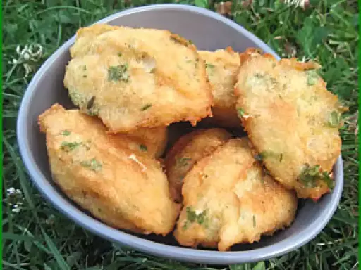 Un bol rempli de beignets de morue portugais dorés, parsemés d'herbes vertes, sur un fond d'herbe.