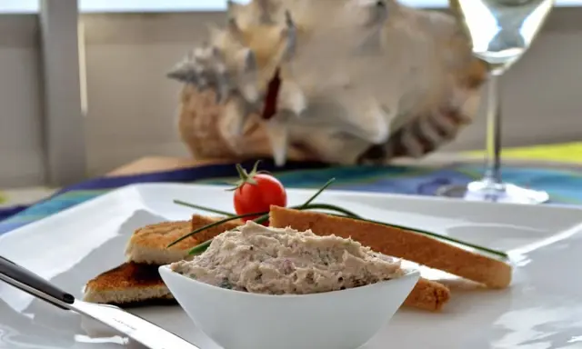 Un bol de rillettes de maquereau, servi avec des toasts grillés, une tomate cerise et un verre de vin blanc.