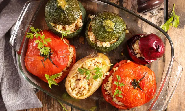 Plat de farce à légume : tomates, courgettes rondes, oignon rouge et pomme de terre farcis de grains, joliment présentés dans un plat en verre.