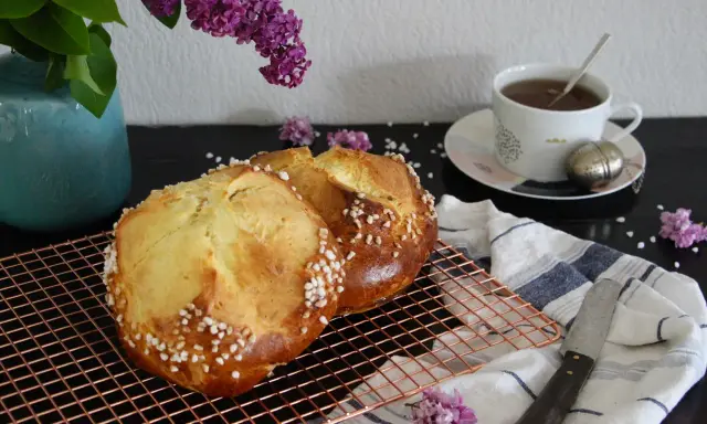 Deux pains briochés, parfaits pour une mouna recette, refroidissent sur une grille. Une tasse de thé et des lilas complètent la scène.