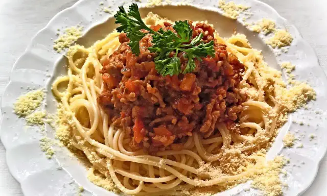 Une assiette de spaghetti bolognaise italienne, garnie de persil frais et de parmesan râpé. Un délice pour les amateurs de cuisine italienne.