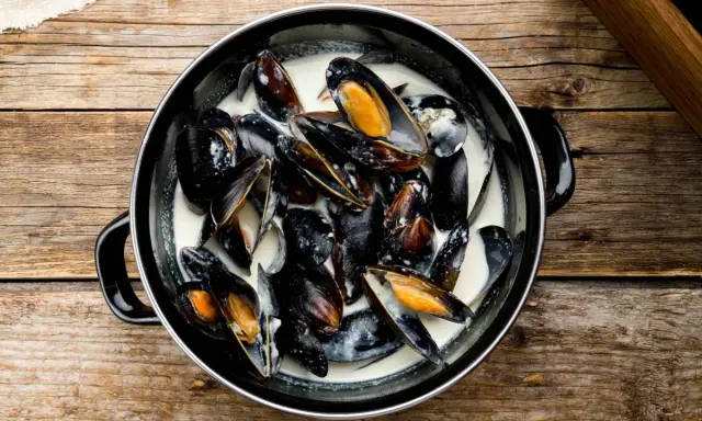 Un plat de moules à la crème, prêtes à être dégustées, sur une table en bois rustique.