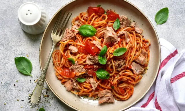 Assiette de pâtes au thon, sauce tomate et basilic frais. Un plat simple et savoureux prêt à être dégusté.