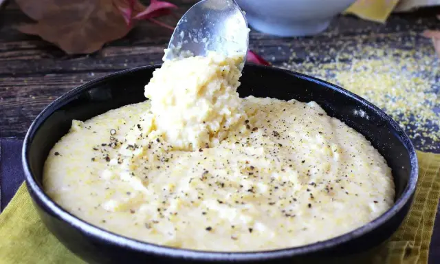 Une cuillère sert une portion généreuse de polenta crémeuse, assaisonnée de poivre noir, dans un bol. Une recette polenta réconfortante.