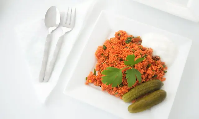 Un plat de boulgour coloré, garni de persil frais, servi avec des cornichons et une touche de yaourt. La cuisson du boulgour est parfaite pour ce repas.