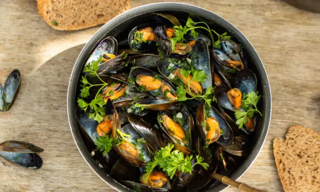 Un plat généreux de moules marinières, garni de persil frais, avec du pain de campagne à côté.