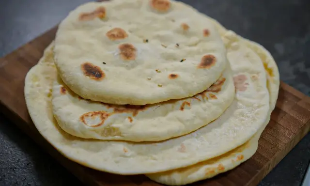 Pile de pains arabes moelleux, légèrement dorés par la cuisson, sur une planche en bois. Parfait pour accompagner un repas.